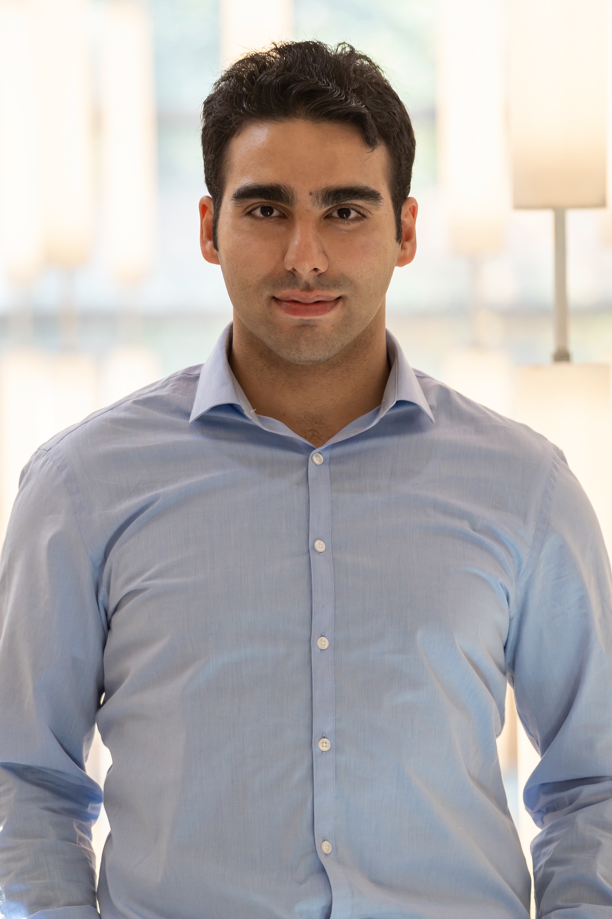 Professor Amir Rahmati: A young man with dark hair and a light blue, collared shirt stands with his hands in his pockets.