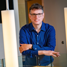 Man wearing glasses and a blue shirt poses behind hanging pendant lights